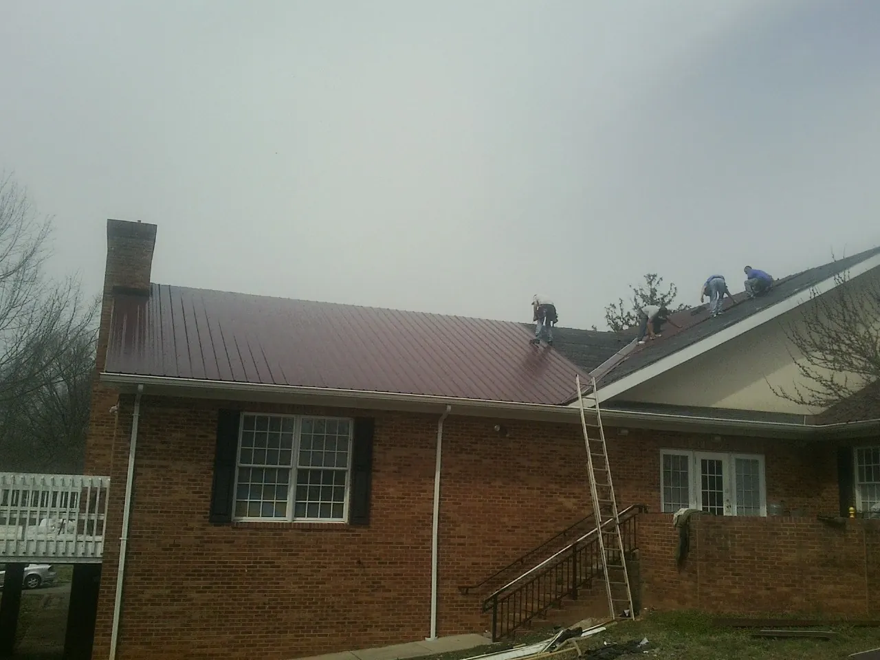 Crew setting red metal roofing panels on a brick home in Taylorsville