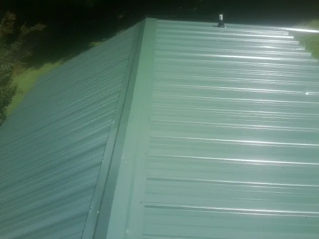 New green metal panels meeting at the ridge of a roof — Flat Roof Repair work by our crew in Taylorsville